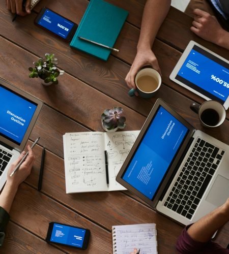Top view of a diverse team using technology in a meeting. Laptops, tablets, and smartphones on a wooden table.